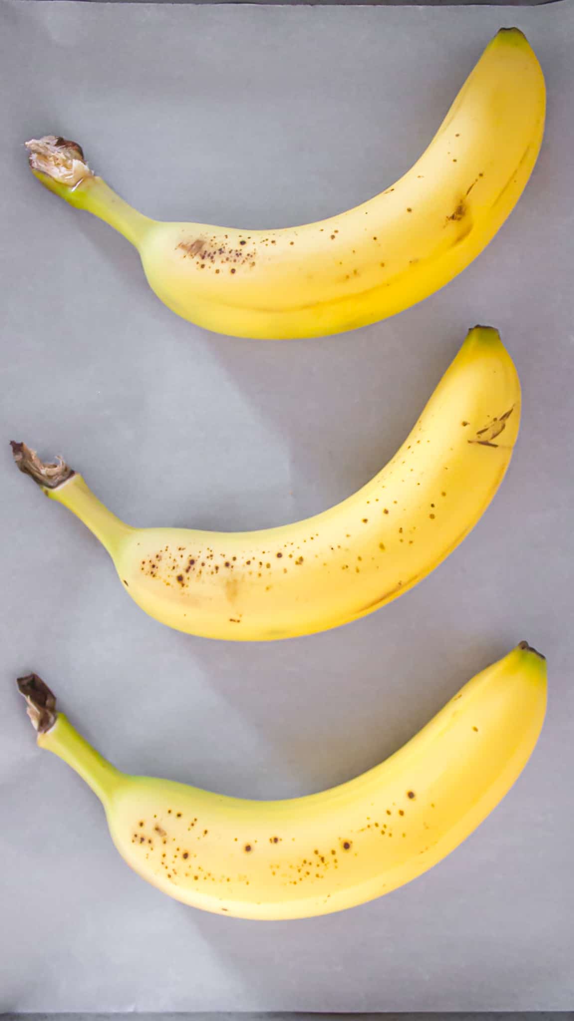 Three unripened bananas on a baking sheet
