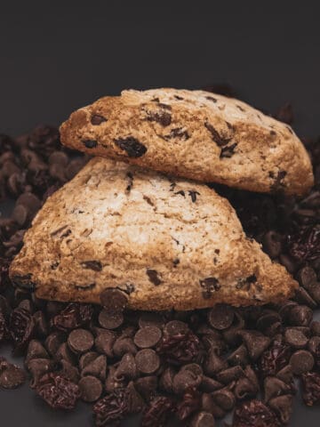 two cherry chocolate scones on top of a pile of chocolate chips and dried cherries