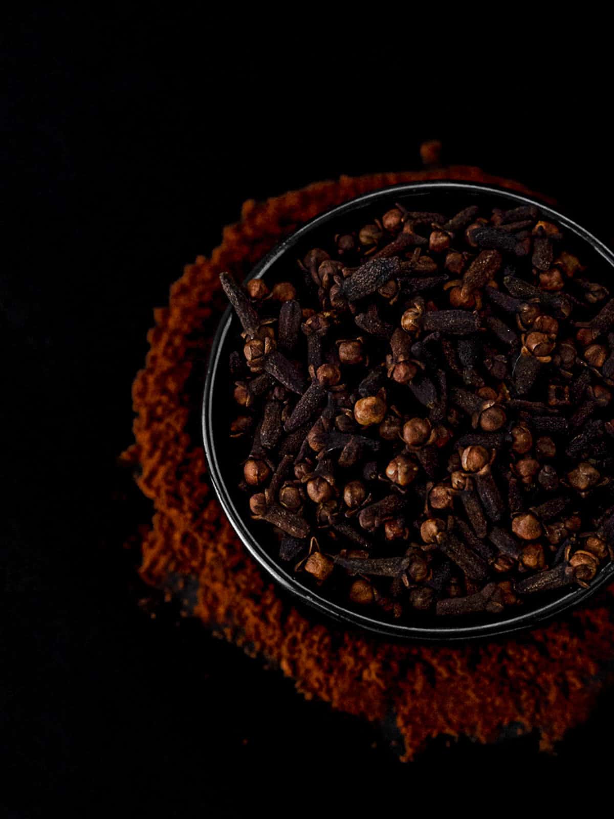 whole cloves in a cup surrounded by ground cloves