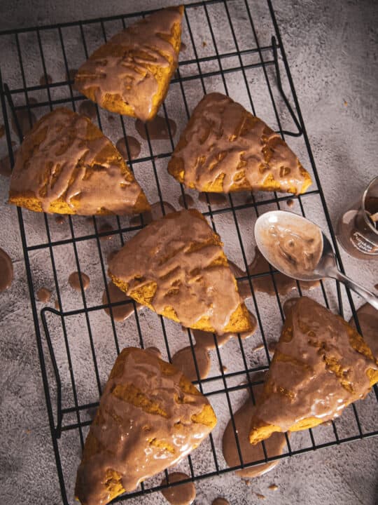 overhead of pumpkin scones on a cooling rack being drizzled with glaze