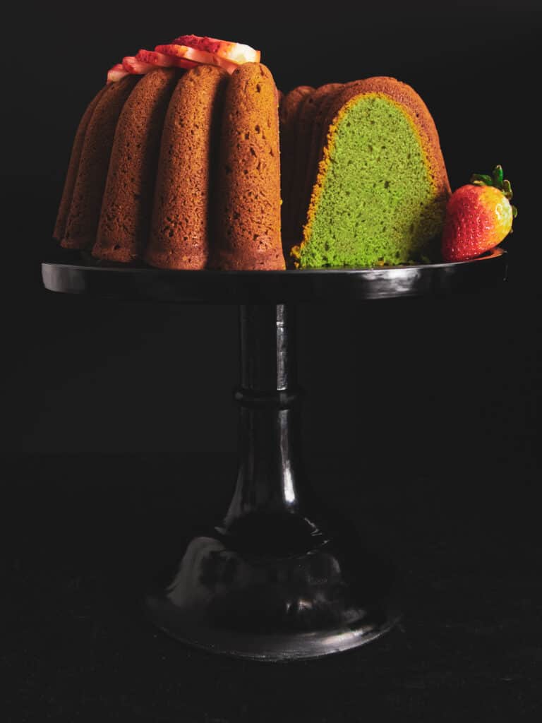matcha cake on a cake stand with a slice taken out.