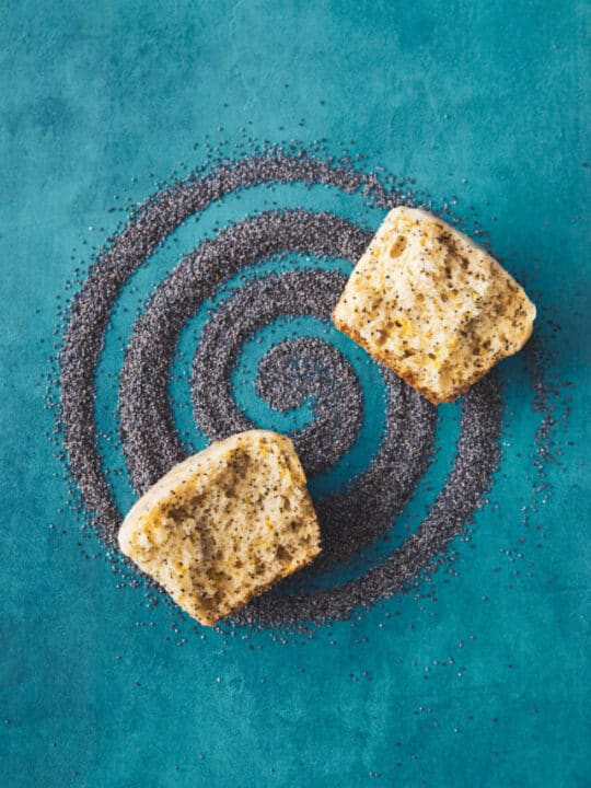 lemon poppy seed muffins laying on a swirl of poppy seeds.