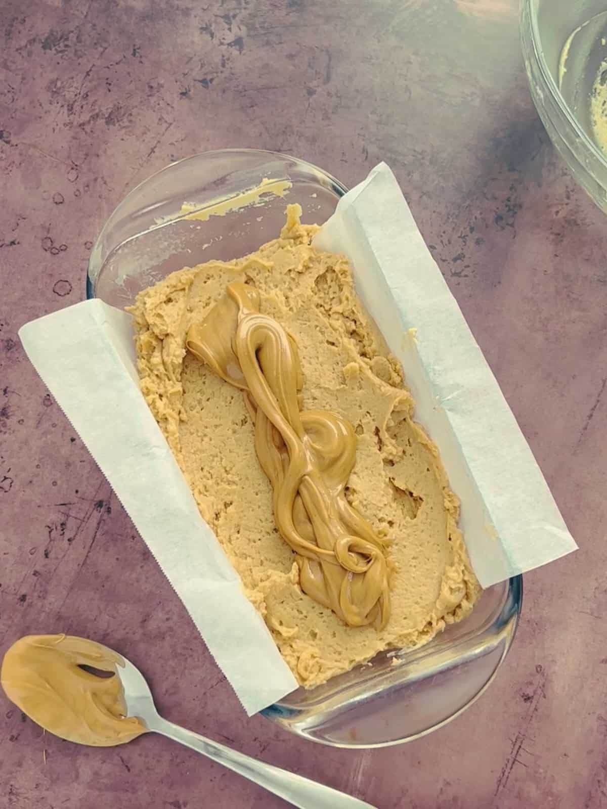 peanut butter bread batter in the loaf pan, topped with slightly melted peanut butter.