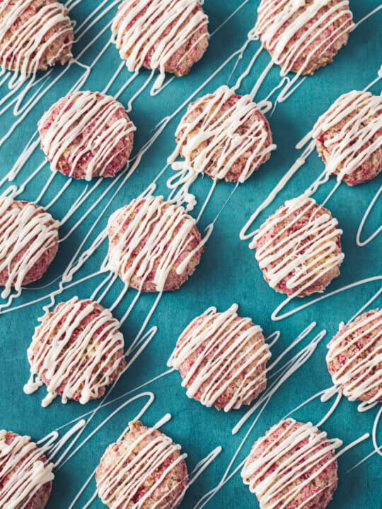 Rows of raspberry cookies drizzled with white chocolate.