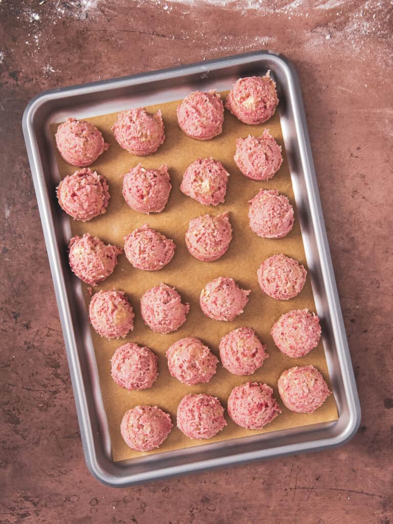 baking sheet is full of cookie dough balls.