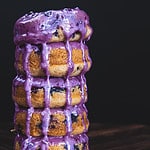A stack of 5 blueberry donuts with blueberry glaze pouring over them.