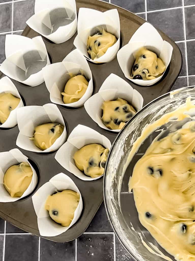Blueberry muffin batter being poured into muffin liners.