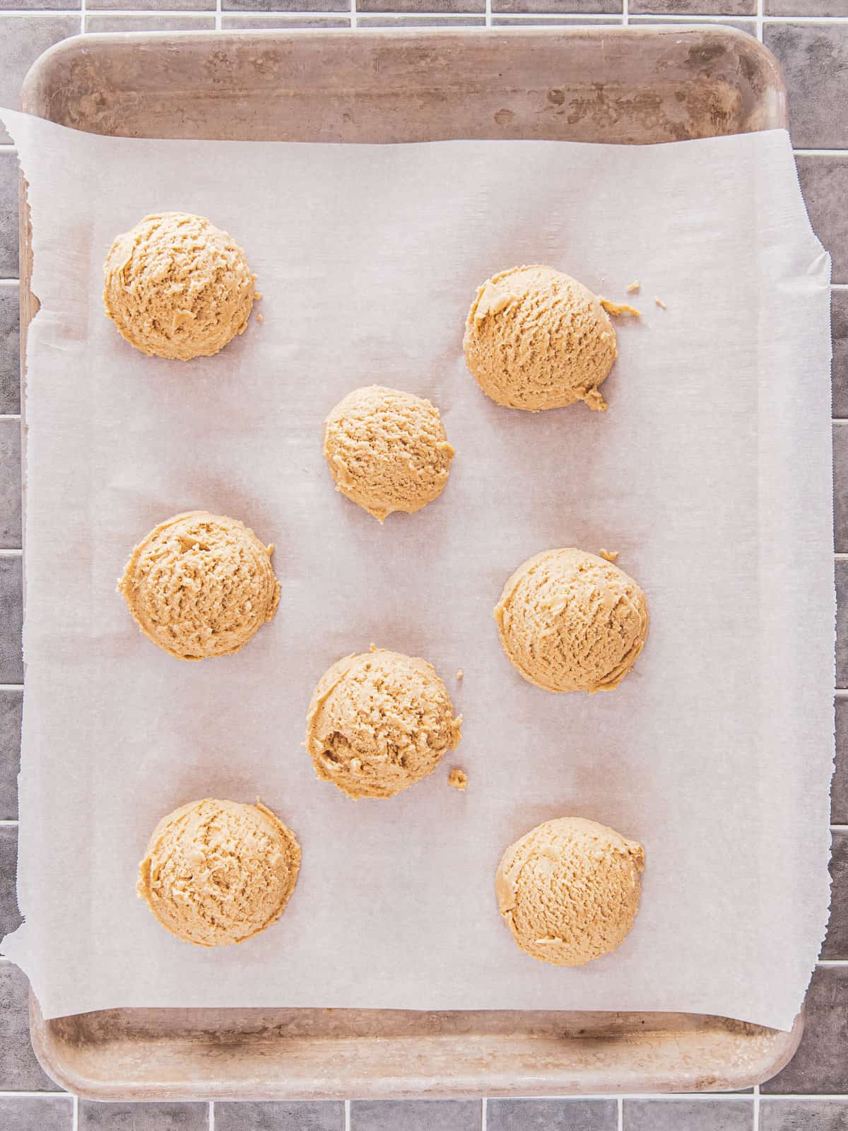 8 cookie dough balls on a parchment lined baking sheet.
