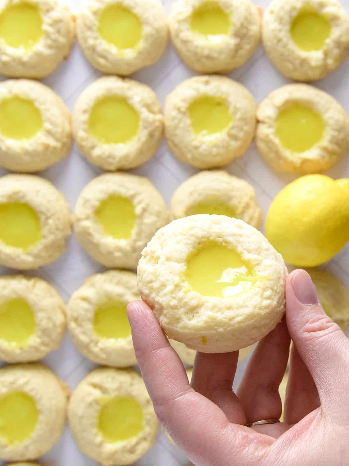 lemon curd thumbprint cookies in a row, while holding one.